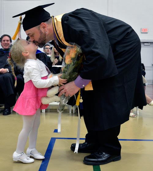 Image of a graduating father leaning down and kissing his young child